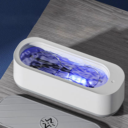 White portable eyeglass and jewelry cleaner machine with a soft blue light, on a wooden table